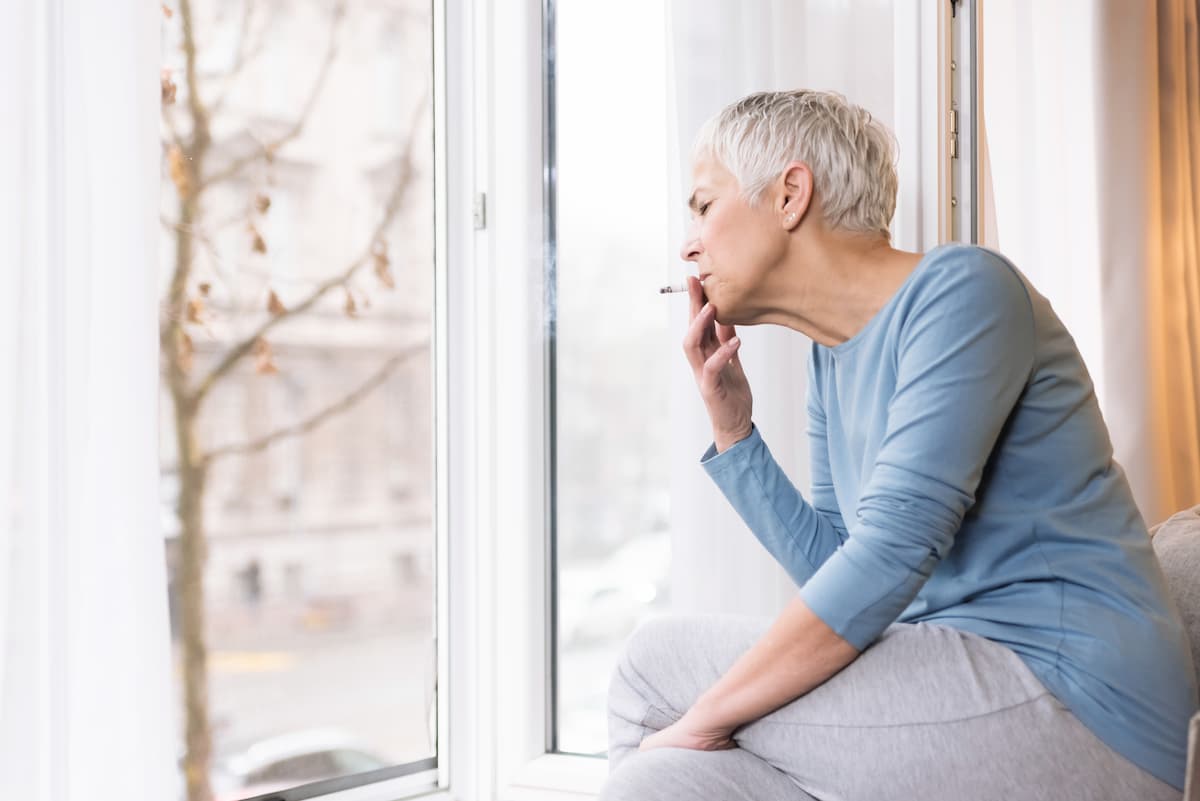 senior fumant une cigarette à la fenêtre